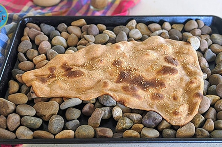 یک نانوای چینی با استفاده از ظرف مخصوص و سنگ، نان سنگک پخت کرده است.